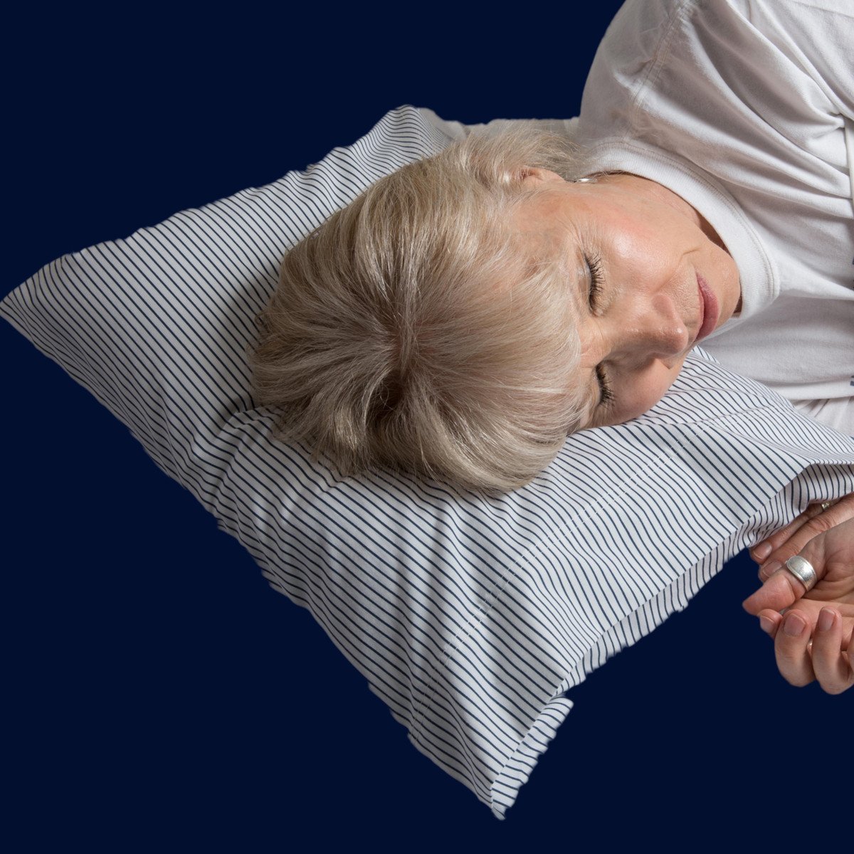 A women is sleeping comfortably on a Pillowpacker inflatible travel pillow in a crisp Navy on white home-style pillowcase